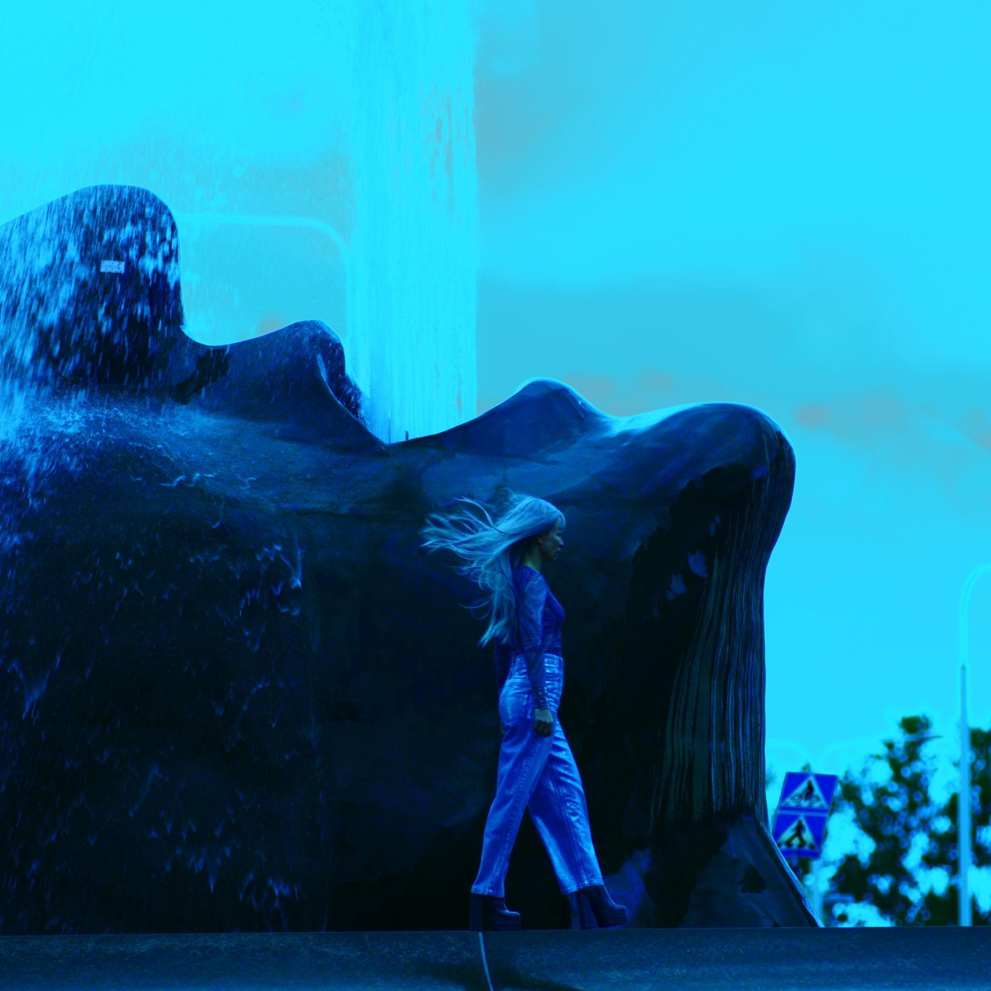Bild från föreställningen Drömspel, föreställandes en kvinna med långt hår som går framför ett berg där ett vattenfall rinner.