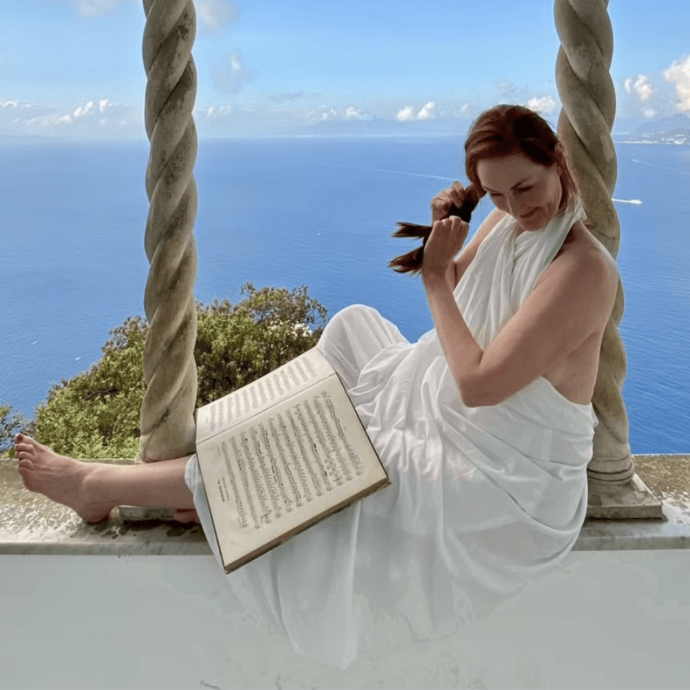 Kvinna som läser bok och flätar håret framöver en vy av hav